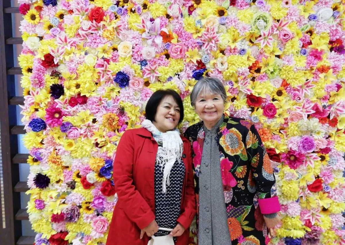 Rei and her mother Yoko standing in front of a wall of flowers